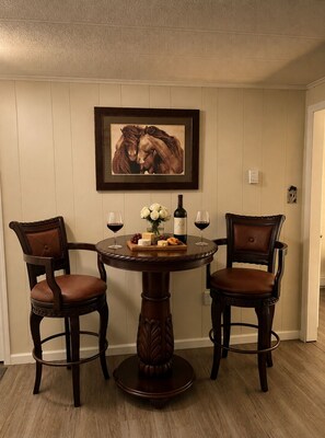 Un coin repas avec une table ronde, deux chaises, une œuvre d’art encadrée et une bouteille de vin.