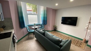 En stue med sofa, et lille bord og et fjernsyn ophængt på væggen.