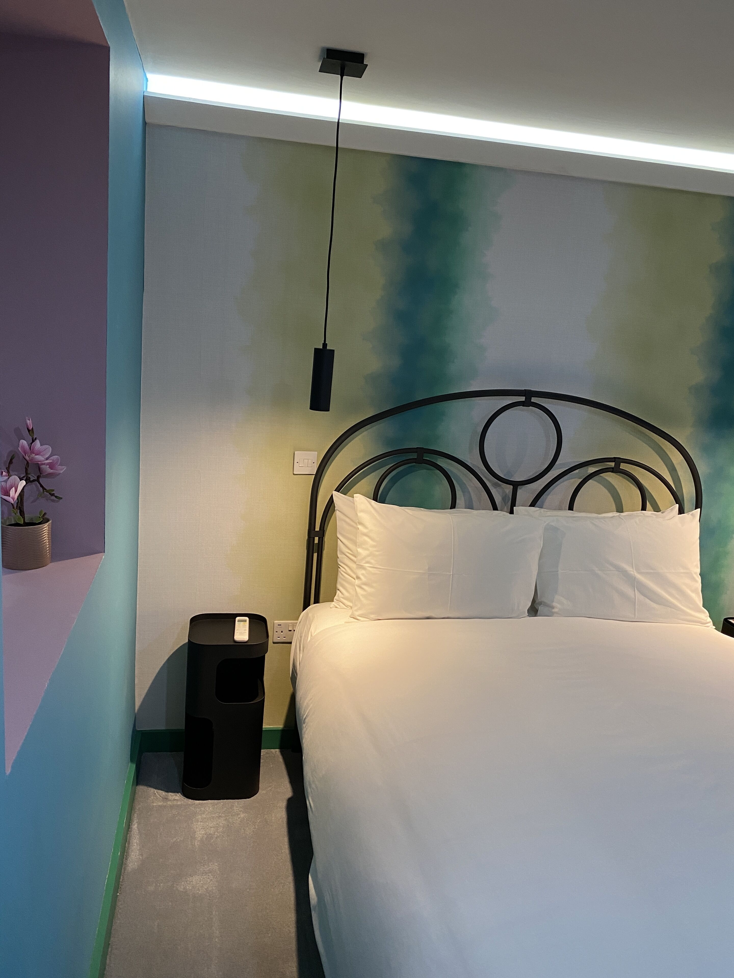 Ein ordentlich bezogenes Bett mit weißer Bettwäsche in einem Zimmer mit grüner und blauer Wand.