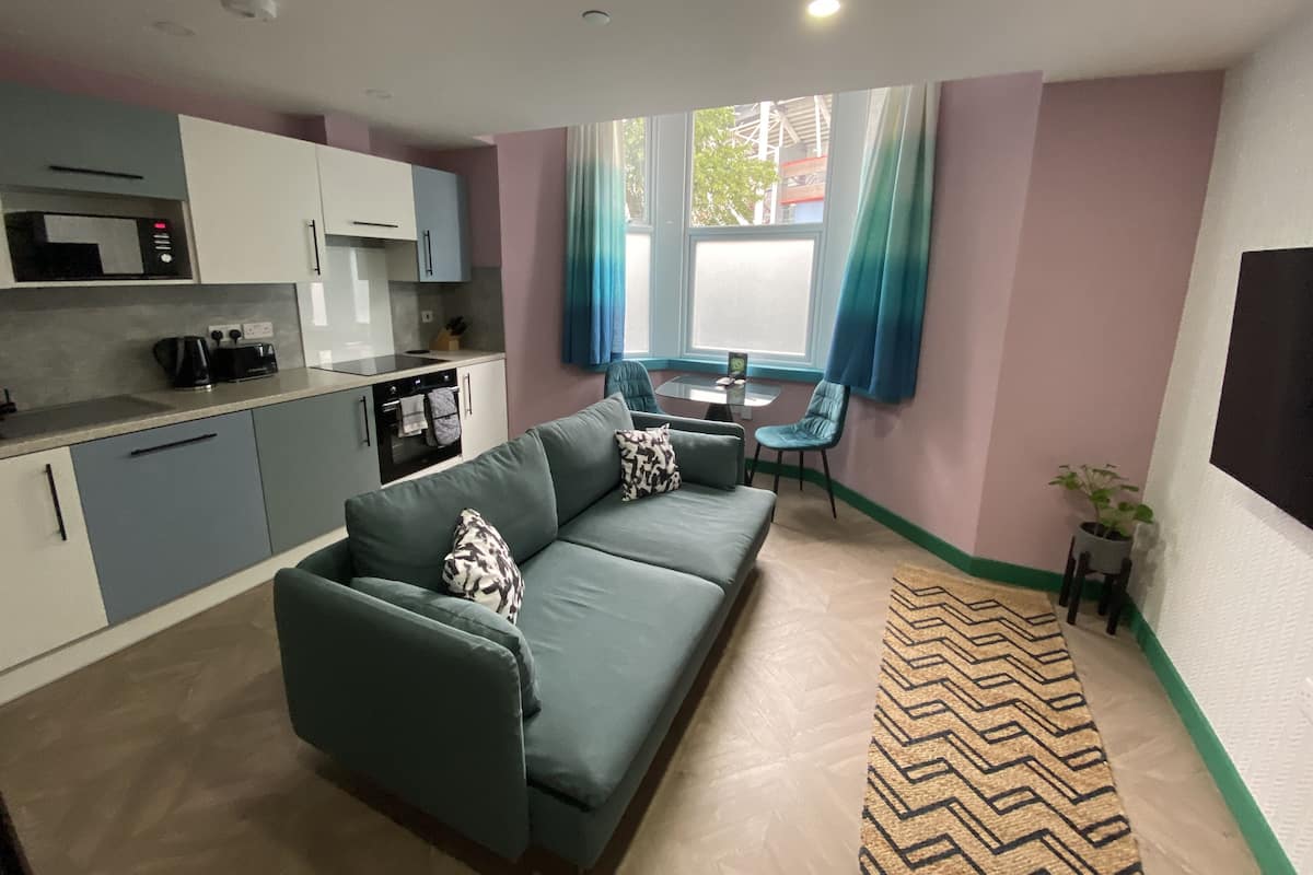 A compact living space with a kitchenette, a sofa, a dining table, and a view of a building outside.