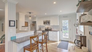 A modern kitchen with white cabinetry, a central island with bar stools, a built-in microwave, and a coffee machine. - Coastal Farmhouse Comfort (Mt Pleasant)