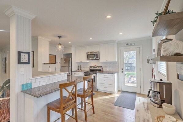 A modern kitchen with white cabinetry, a central island with bar stools, a built-in microwave, and a coffee machine.