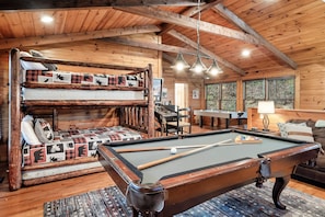 A cozy cabin with a pool table, a bunk bed with plaid bedding, and a rustic wooden interior.