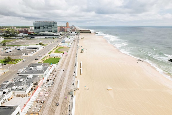 A coastal cityscape with a wide beach, a road parallel to the shore, and buildings including a large hotel. - Pet Friendly 1.5BR 2 Blocks to Beach & Main Ave | Full Kitchen | Near Asbury (Ocean Grove)