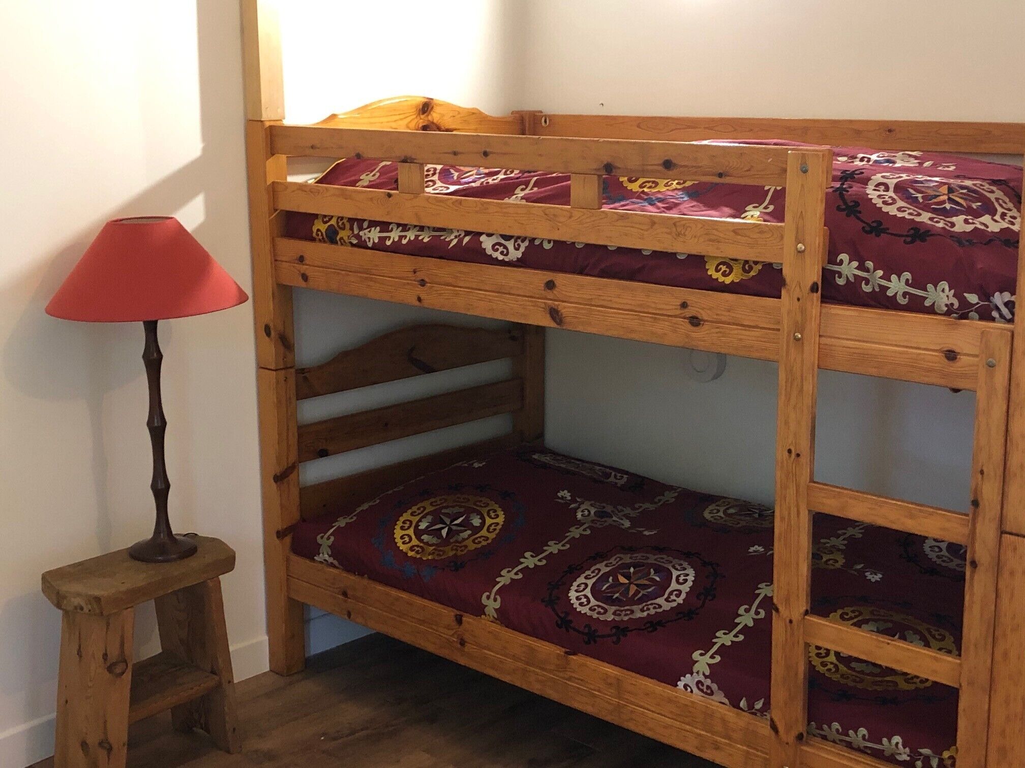 A bunk bed with patterned bedding, a small wooden stool, and a red lamp.