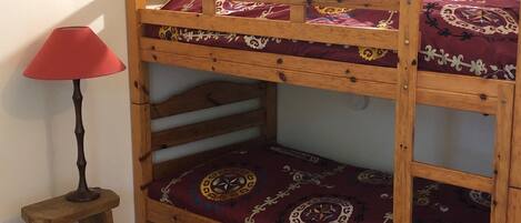 A bunk bed with patterned bedding, a small wooden stool, and a red lamp.