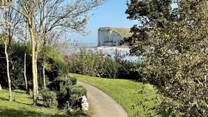 Un sentier pavé dans un parc, bordé d’arbres, d’où l’on aperçoit une grande falaise au loin.