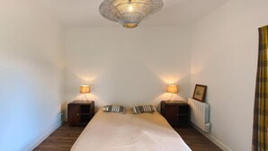 Une chambre à coucher avec un grand lit, deux tables de chevet avec des lampes, un radiateur et un luminaire suspendu.