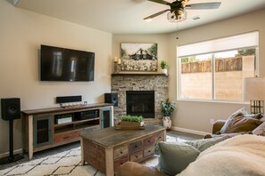 A living room with a stone fireplace, a mounted TV, and a ceiling fan. - Sandia Velo- New Modern Farmhouse Style Home (Albuquerque)