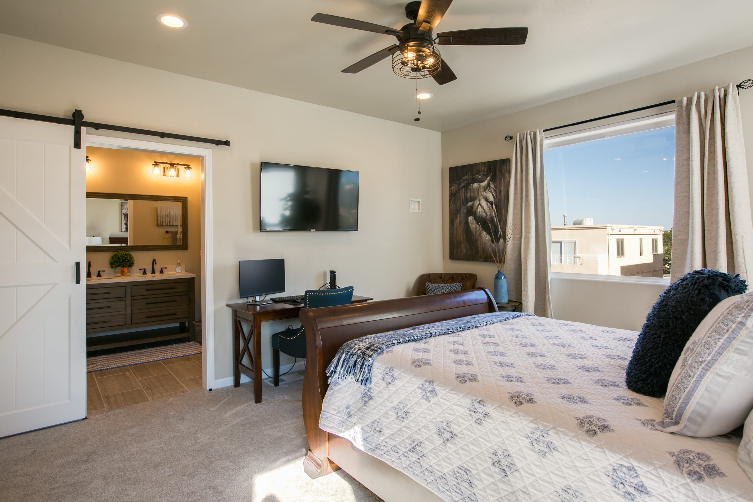 A bedroom with a bed, a desk, a chair, a television, and a ceiling fan.