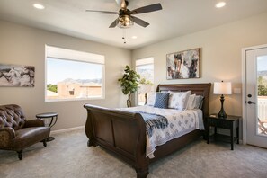A bedroom with a large bed, a ceiling fan, a chair, a small table, and a nightstand with a lamp. - Sandia Velo- New Modern Farmhouse Style Home (Albuquerque)