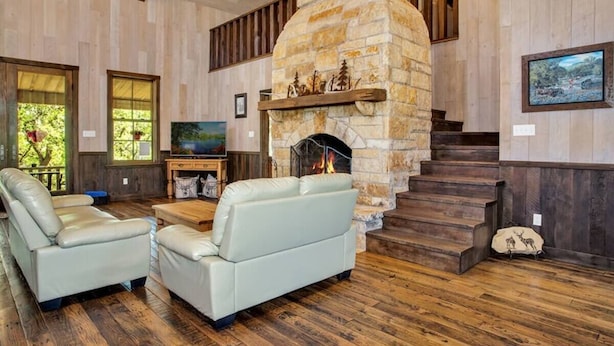 A cozy living room with a stone fireplace, leather sofas, and a wooden floor.