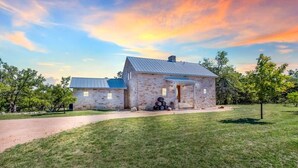 A stone house with a metal roof, a paved driveway, and a grassy yard.