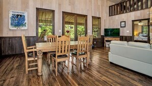 A wooden-paneled room with a dining table and chairs, a white sofa, and a television.