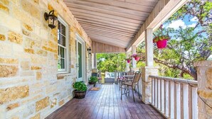 A wooden porch with stone walls, outdoor seating, and hanging flower pots.