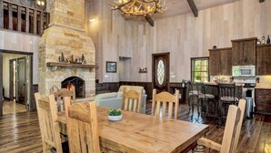 A spacious living room with a stone fireplace, wooden dining table, and chairs.