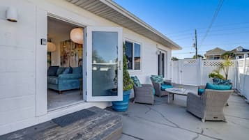 A covered patio with outdoor furniture, a sliding glass door entrance, and a white fence.