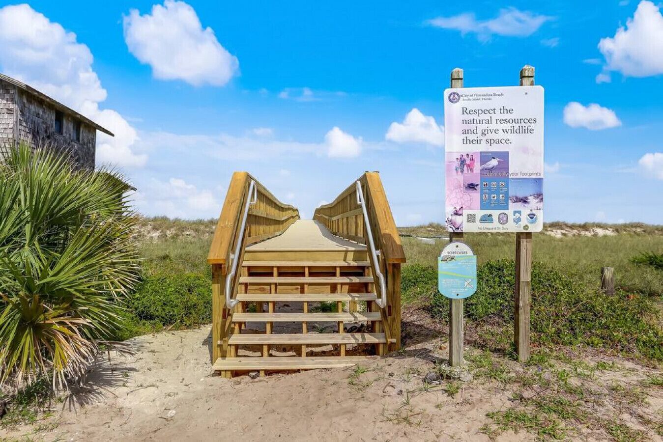 Een houten looppad dat naar de ingang van een strand leidt, met een bord met informatie over natuurbescherming.
