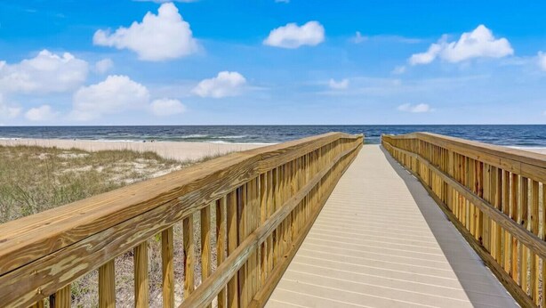 Una passerella di legno che conduce alla spiaggia, con una vista aperta sull'oceano e sul cielo.