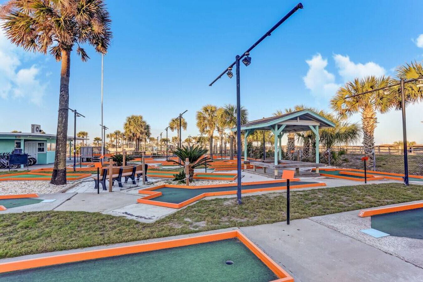 Een minigolfbaan met oranje en groene speelvelden, bankjes en een kiosk.