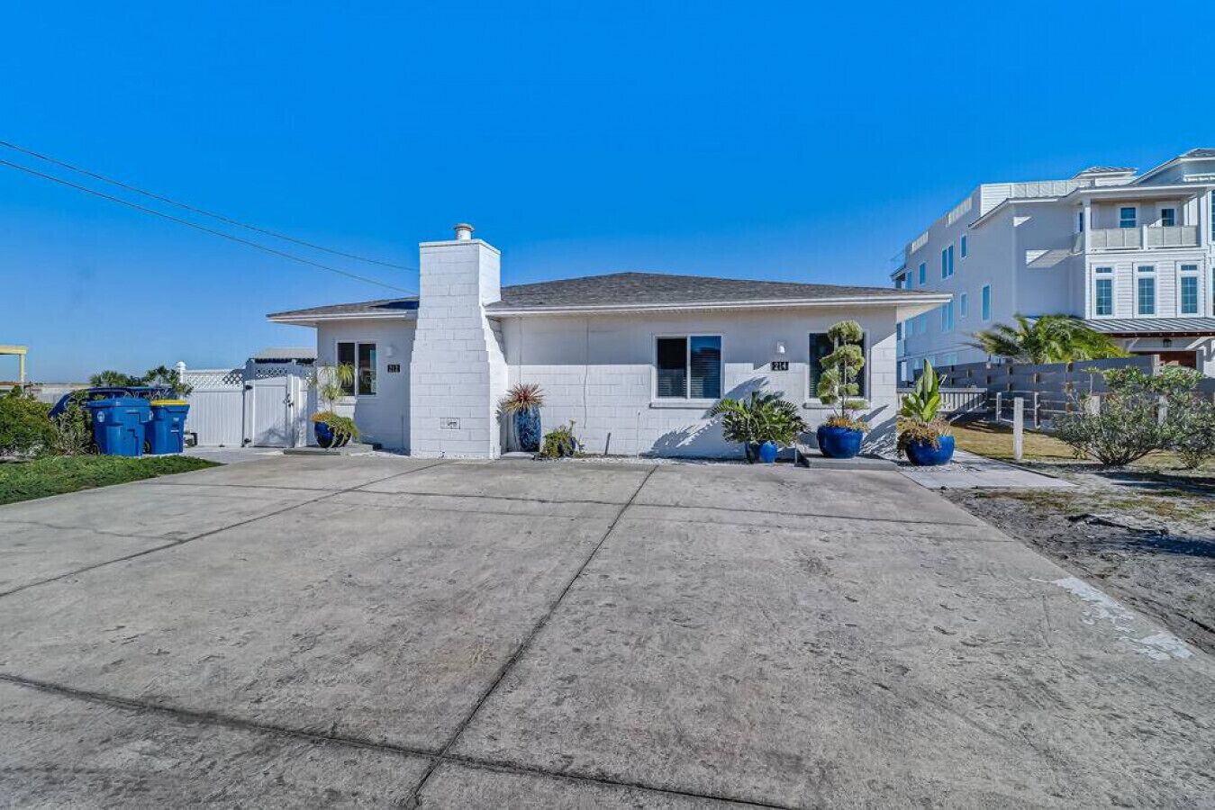 A single-story house with a garage, a small porch with potted plants, and a clear blue sky.
