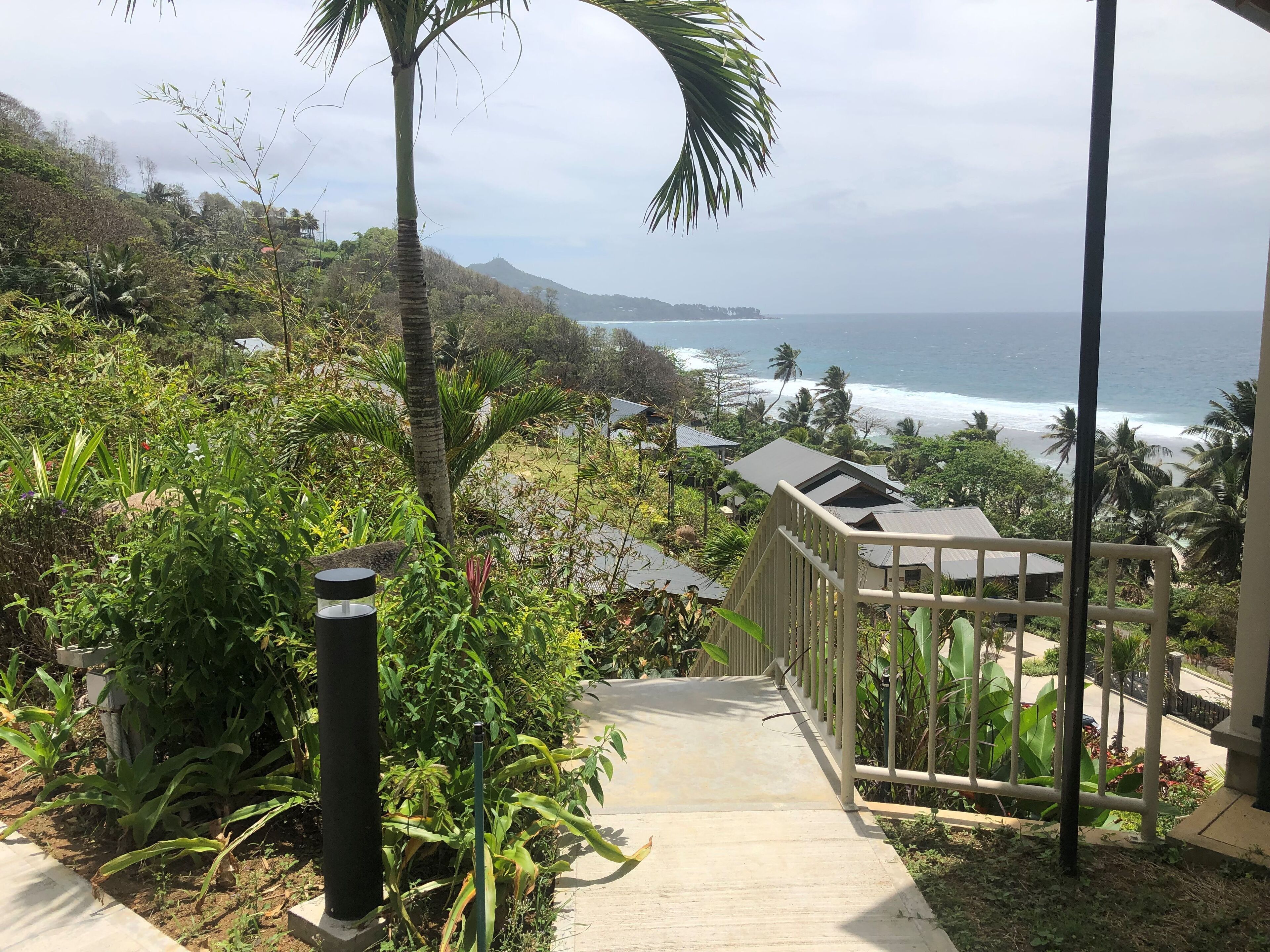 A pathway leading to a building with a view of the ocean and a tropical landscape.
