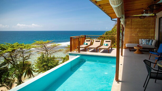 A pool area with lounge chairs and a view of the ocean.