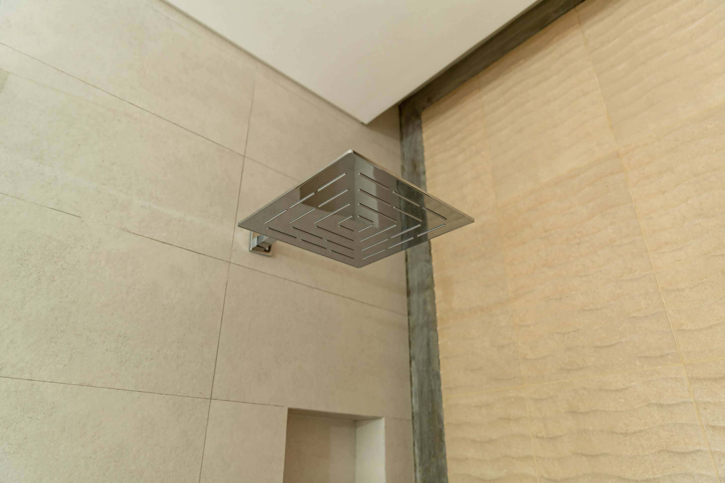 Une salle de bain moderne avec une pomme de douche carrée et un mur à texture.