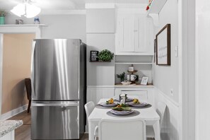 A modern kitchen with a stainless steel refrigerator, white cabinetry, and a dining table set with plates and sunflowers.