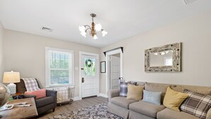A living room with a sofa, a coffee table, a patterned rug, a chandelier, and a mirror on the wall. - Genevieve's Cottage! Totally Renovated with all the Charm! (Hixson)