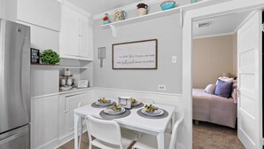 A compact kitchen with white cabinetry, a built-in refrigerator, and a dining area with a white table set for four. A framed quote is displayed on the wall above the dining table. - Genevieve's Cottage! Totally Renovated with all the Charm! (Hixson)