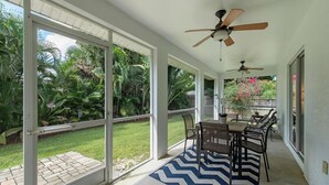 Un patio techado con zona de comedor, ventiladores de techo y vistas a un jardín exuberante.