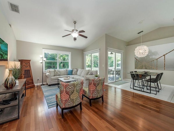 A spacious living room with hardwood flooring, a ceiling fan, and a large window.