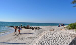 A beach with people walking and sitting, a rocky shoreline, and calm sea.