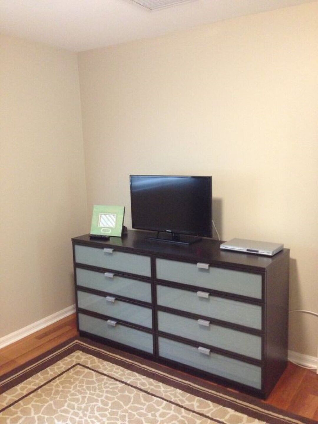 A room with a dark wooden dresser, a television on top, and a small green sign.