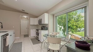Una cocina moderna con armarios blancos, un microondas y un comedor con una mesa y sillas de vidrio.