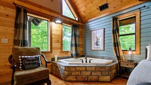 Ein Badezimmer einer Holzhütte mit einer Steinebadewanne, einem Holzstuhl mit Kissen und einer gerahmten Karte an der Wand.