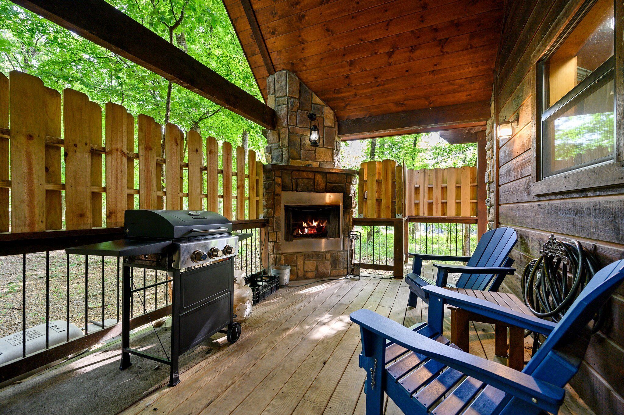 A covered outdoor area with a stone fireplace, wooden deck, and Adirondack chairs.