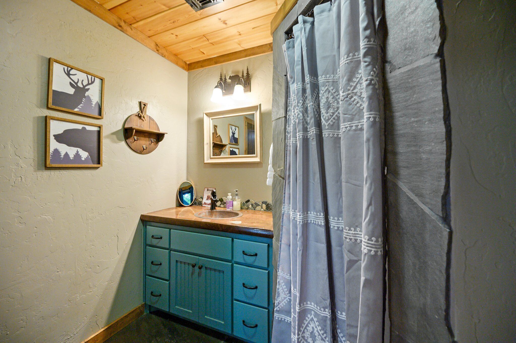 A bathroom with a wooden ceiling, a sink with a mirror, and two framed pictures on the wall.