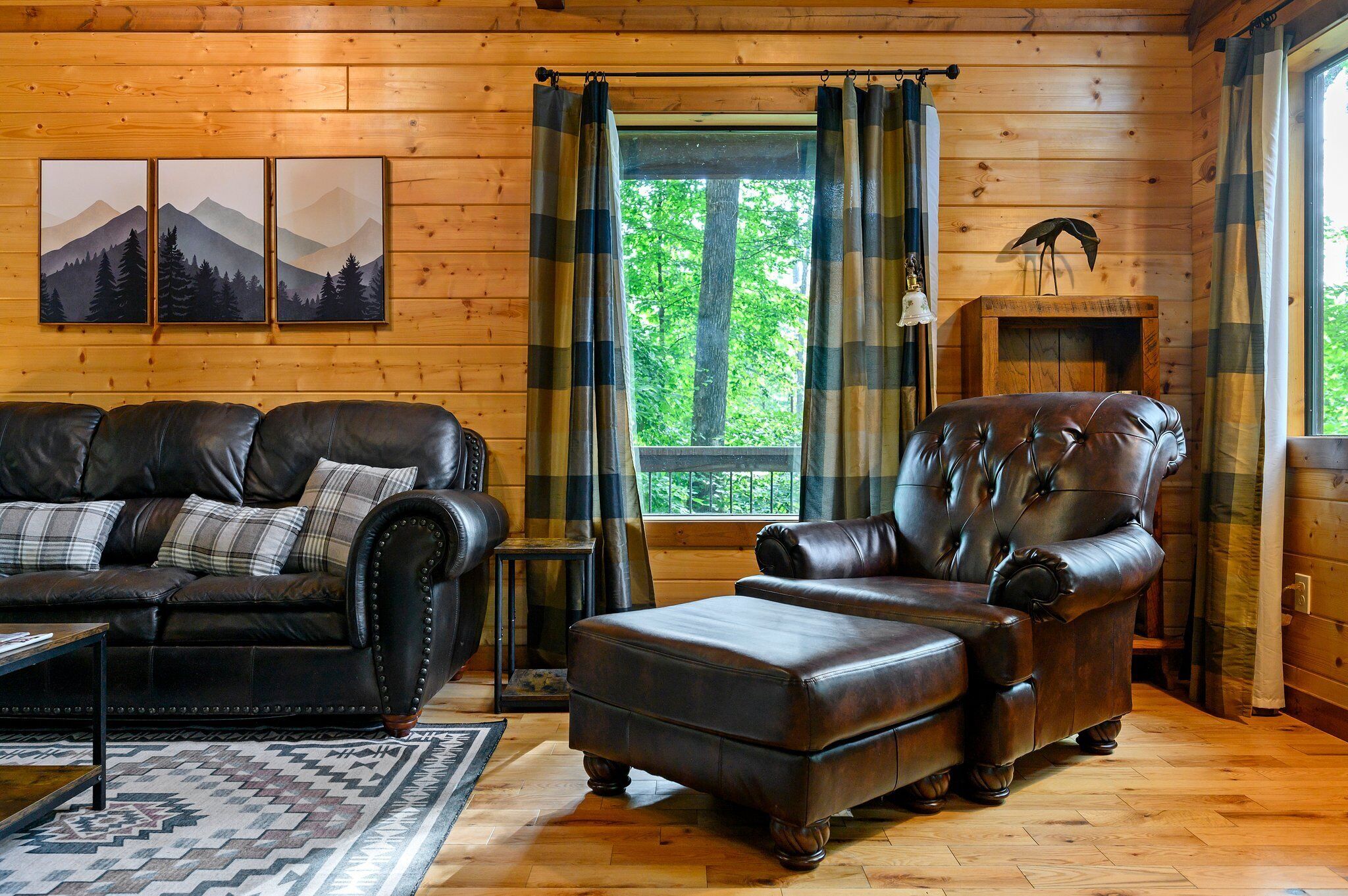 A cozy log cabin interior with a leather sofa, a matching armchair, and a fireplace.