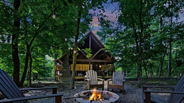 Eine Hütte mit einem Steinkamin und zwei Adirondack-Stühlen davor.