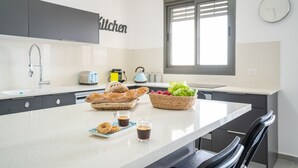 A modern kitchen with a large island, a toaster, a kettle, and a basket of fresh produce.