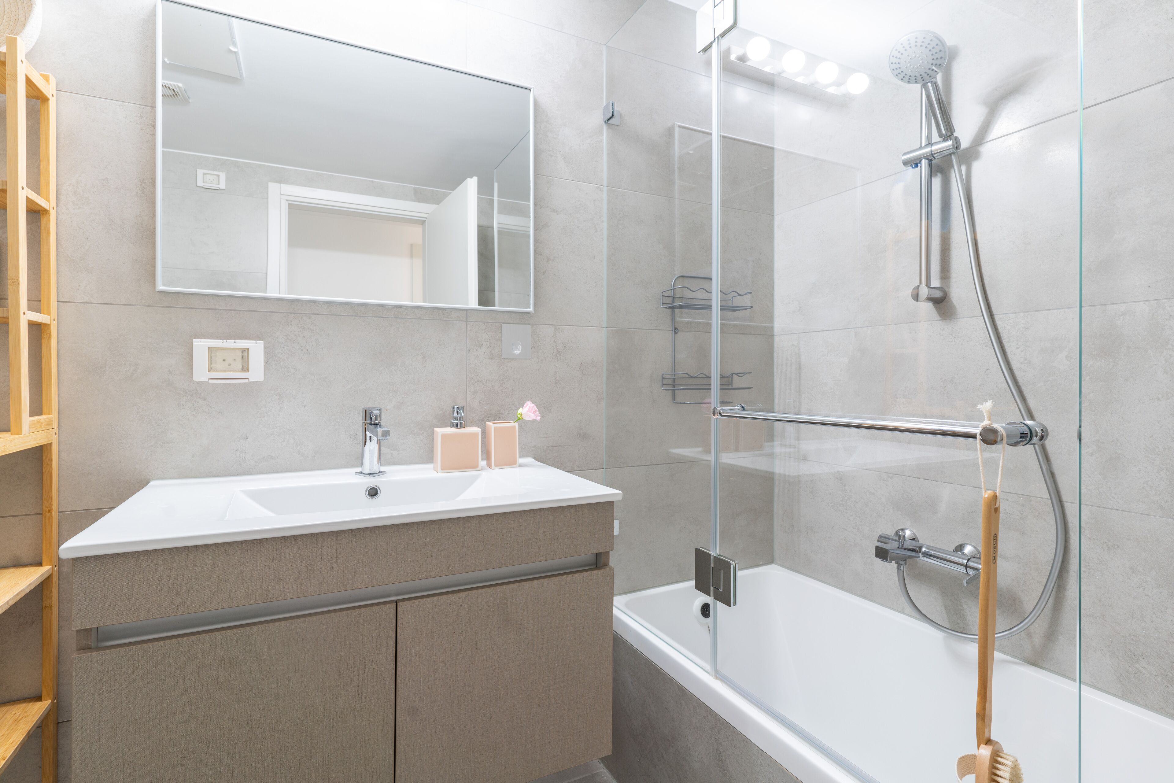 Un baño moderno con ducha de vidrio, un espejo grande y un lavabo blanco sobre un mueble de madera.