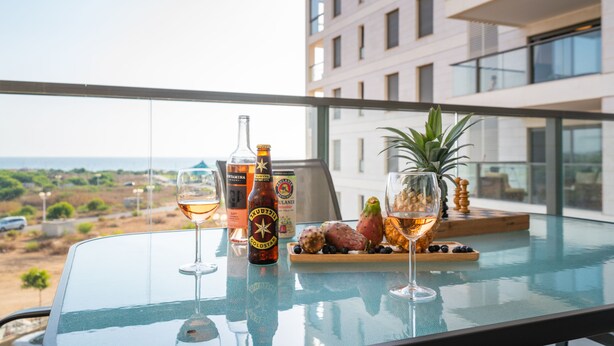 A balcony with a glass table set with drinks, a bottle, and fruit.