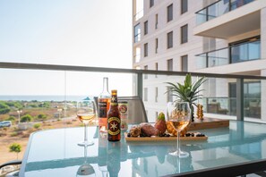 A balcony with a glass table set with drinks, a bottle, and fruit.