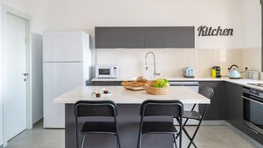 A modern kitchen with a central island, two black chairs, a microwave, a toaster, and a kettle.