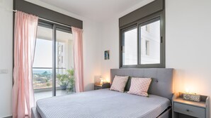 A bedroom with a bed, a nightstand, a window, and a view of buildings.