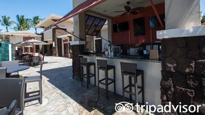 Un espace patio avec des sièges d’extérieur, un bar avec des tabourets et un mur en pierre.