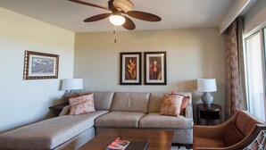 A living room with a sofa, a coffee table, a ceiling fan, and framed artwork on the wall. - Hilton timeshare in Big Island 2 bedroom 2 bath (Waikoloa Village)