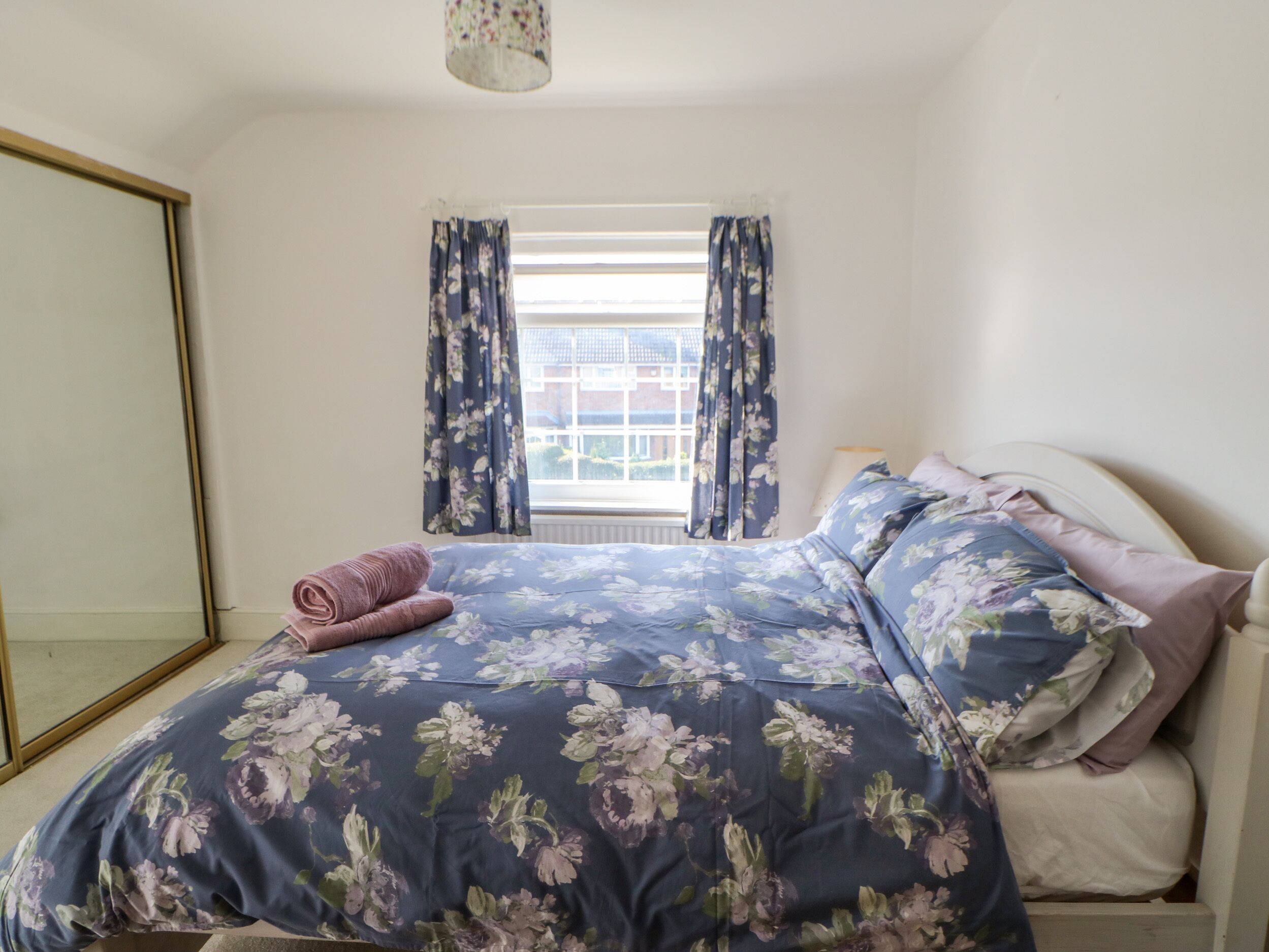 A bedroom with a bed, a window with curtains, and a mirror.